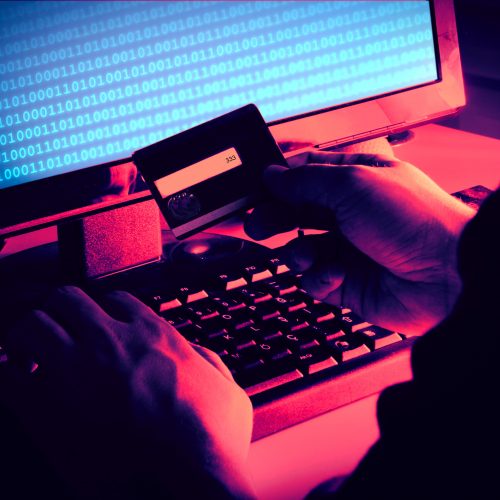 Black hands of anonymous hackers holding credit card and using, typing code on keyboard of laptop for remotely reach, receiving personal information online, Networking Crime Payment Security Concept